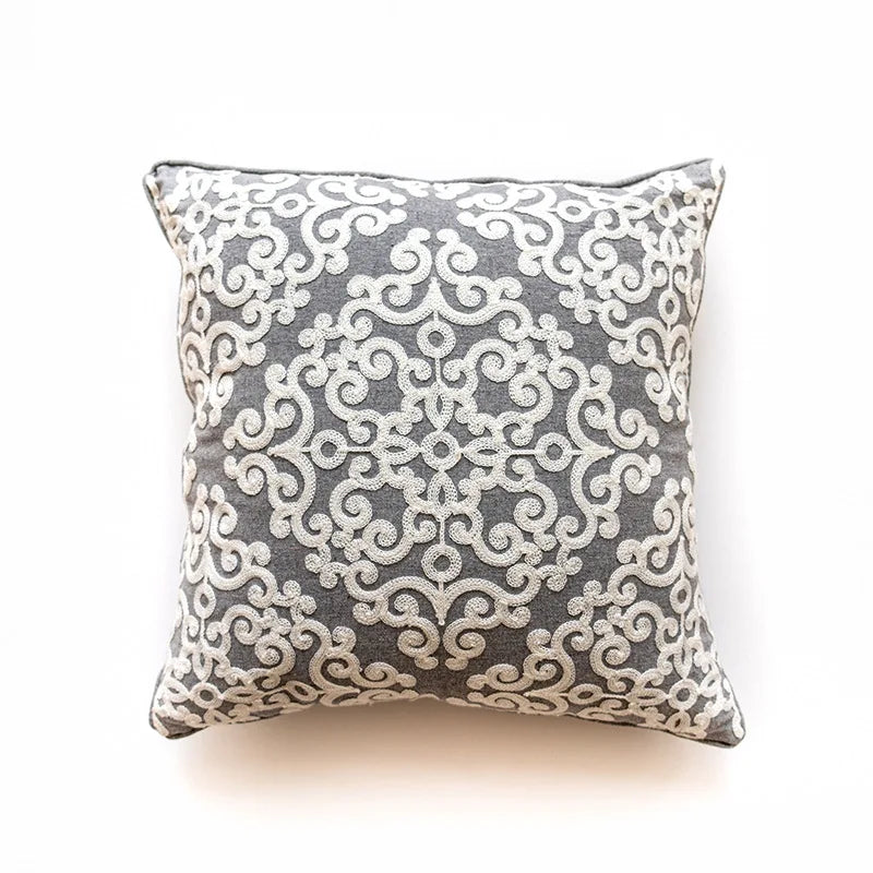 Coussin décoratif gris à motifs damassés blancs.