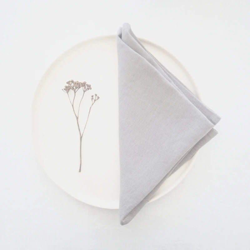 Cette image montre un élément floral sec, une branche d'arbre ou de plante, posé sur un fond blanc, avec un tissu gris clair enroulé à côté.