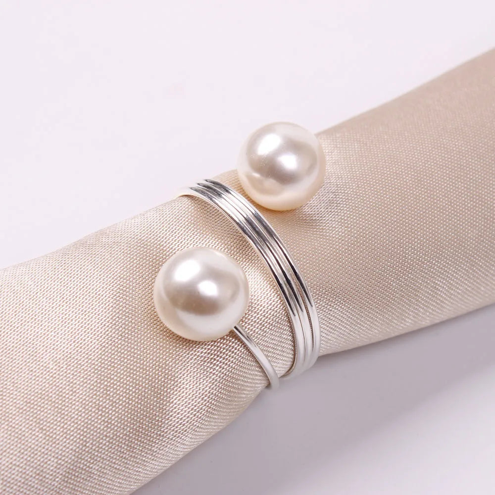 L'image montre un jonc argenté orné de deux perles blanches rondes, posé sur un tissu beige.