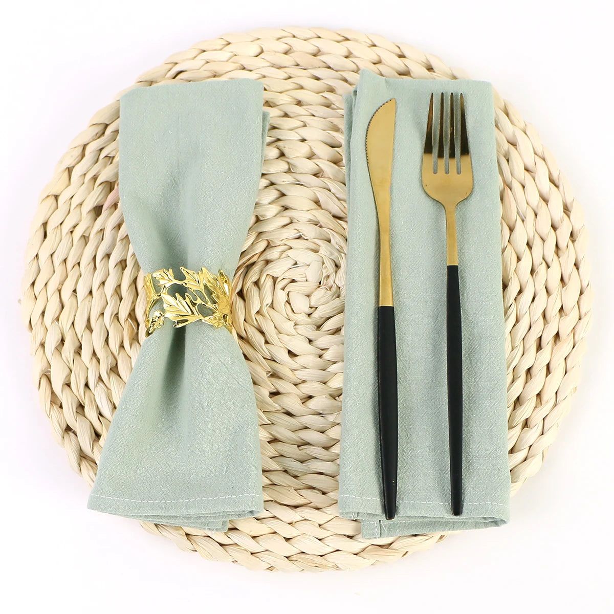 Couverts de table sur un set de table en paille tressée, avec une serviette de table et des couverts dorés sur un fond blanc.