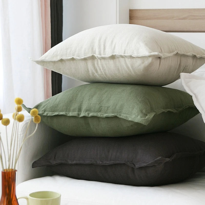 Gros plan sur un lit avec des oreillers blancs et vert olive, et de petites fleurs jaunes à côté.