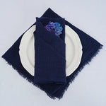 Serviette de table bleue marine ornée d'une fleur bleue et violet sur une assiette blanche, créant une ambiance élégante et raffinée.