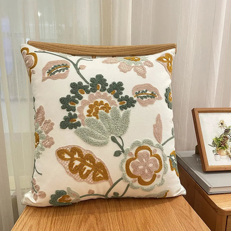 Coussin décoratif en tissu beige avec motifs floraux colorés et broderies élégantes, posé sur un meuble en bois.