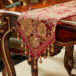 Élégant chemin de table en velours rouge décoré d'un motif floral doré, orné de perles pendantes en métal.
