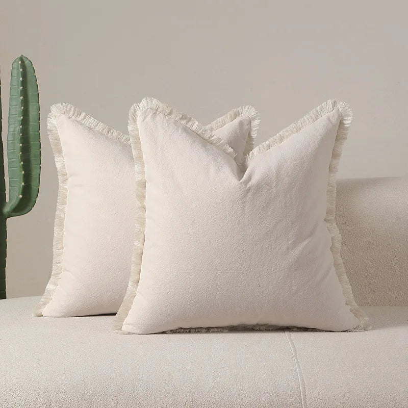 Coussin blanc moelleux avec franges décoratives sur un canapé gris.