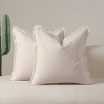 Coussin blanc moelleux avec franges décoratives sur un canapé gris.