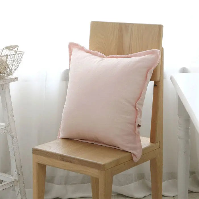 Coussin décoratif en tissu rose pâle posé sur une chaise en bois.