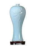 Vase en céramique bleu clair en forme de fleur avec un col étroit et un socle en bois sombre.