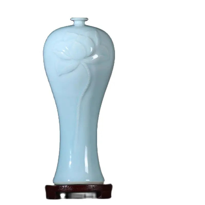Vase en céramique bleu clair en forme de fleur avec un col étroit et un socle en bois sombre.