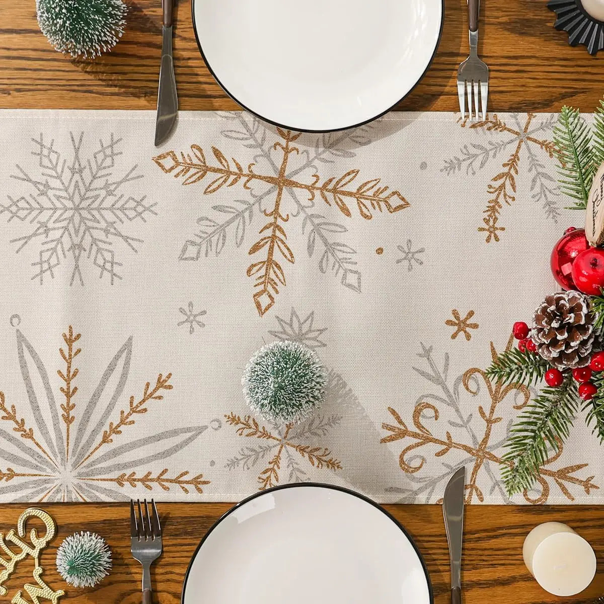 Composition festive de Noël avec des motifs de flocons de neige dorés, des branches de sapin et des détails décoratifs sur une nappe en lin.