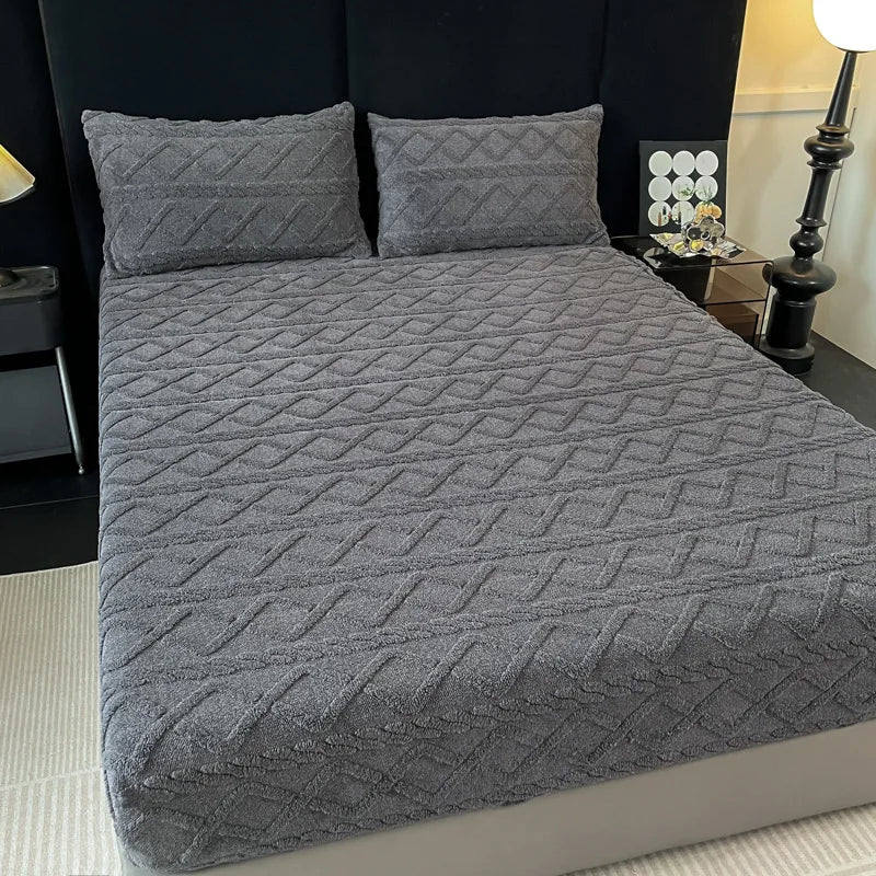 Ensemble de literie gris foncé avec motifs texturés sur le couvre-lit et les oreillers, placé sur un lit avec une table de chevet et une lampe dans une chambre.