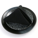 Plat de service rond en céramique noire avec des éléments décoratifs argentés et brillants.