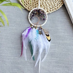 Un attrapeur de rêves décoratif avec un cercle en métal, des plumes multicolores et des pierres d'améthyste disposées avec soin.