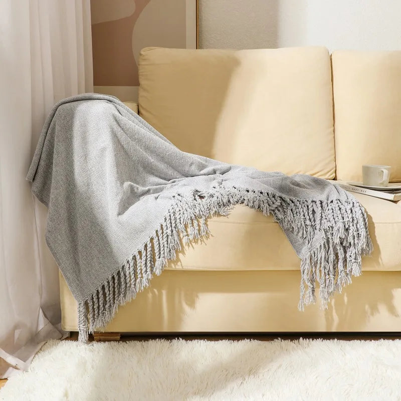 Une couverture grise douce et moelleuse accrochée sur un canapé beige dans un salon cosy.