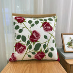 Taie d'oreiller décorative blanche et verte avec des motifs de roses rouges, posée sur un meuble en bois.