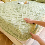 Une couverture moelleuse de couleur vert-olive avec un motif géométrique dessiné sur sa surface, posée sur un lit.