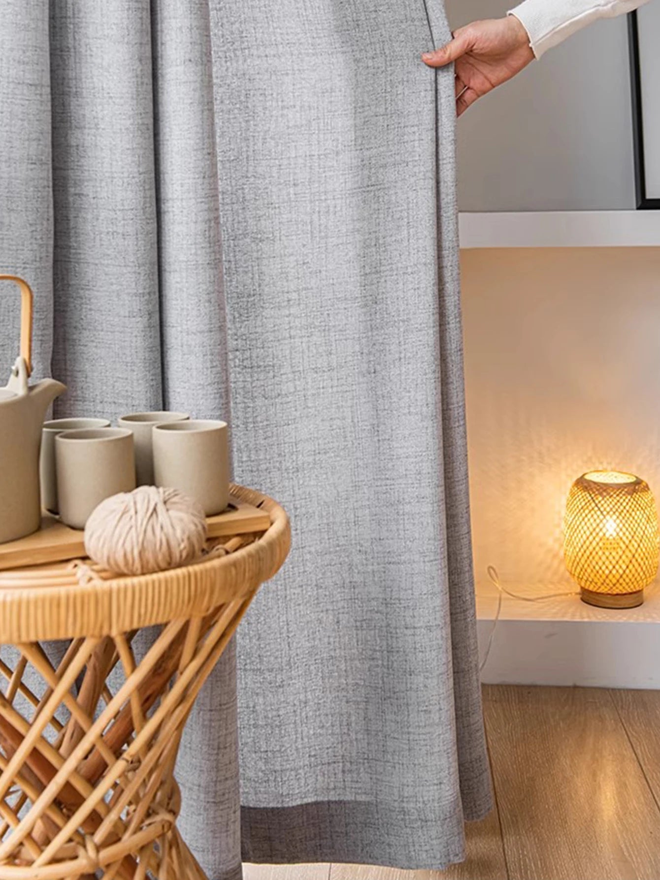Gros plan sur un voilage gris clair tamisant, tenu à la main dans une ambiance cocooning.