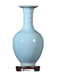 Vase en porcelaine d'un bleu pastel, posé sur un support en bois foncé.