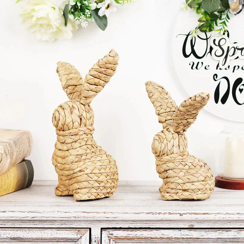 Deux adorables lapins décorés en osier, posés sur une table vintage avec des fleurs blanches, créant une scène printanière chaleureuse et bucolique.