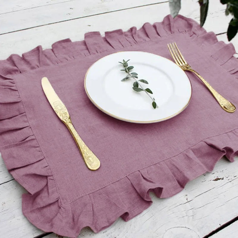 Une élégante table de repas avec une nappe pourpre froissée, une assiette blanche ornée de branches de feuillage et des couverts dorés.