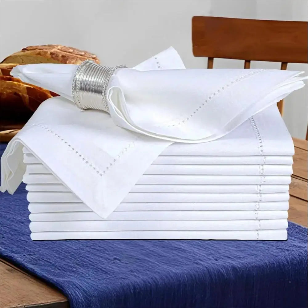 Serviettes de table blanches élégantes avec détails décoratifs sur une nappe bleue froissée, accompagnées d'un pain frais.
