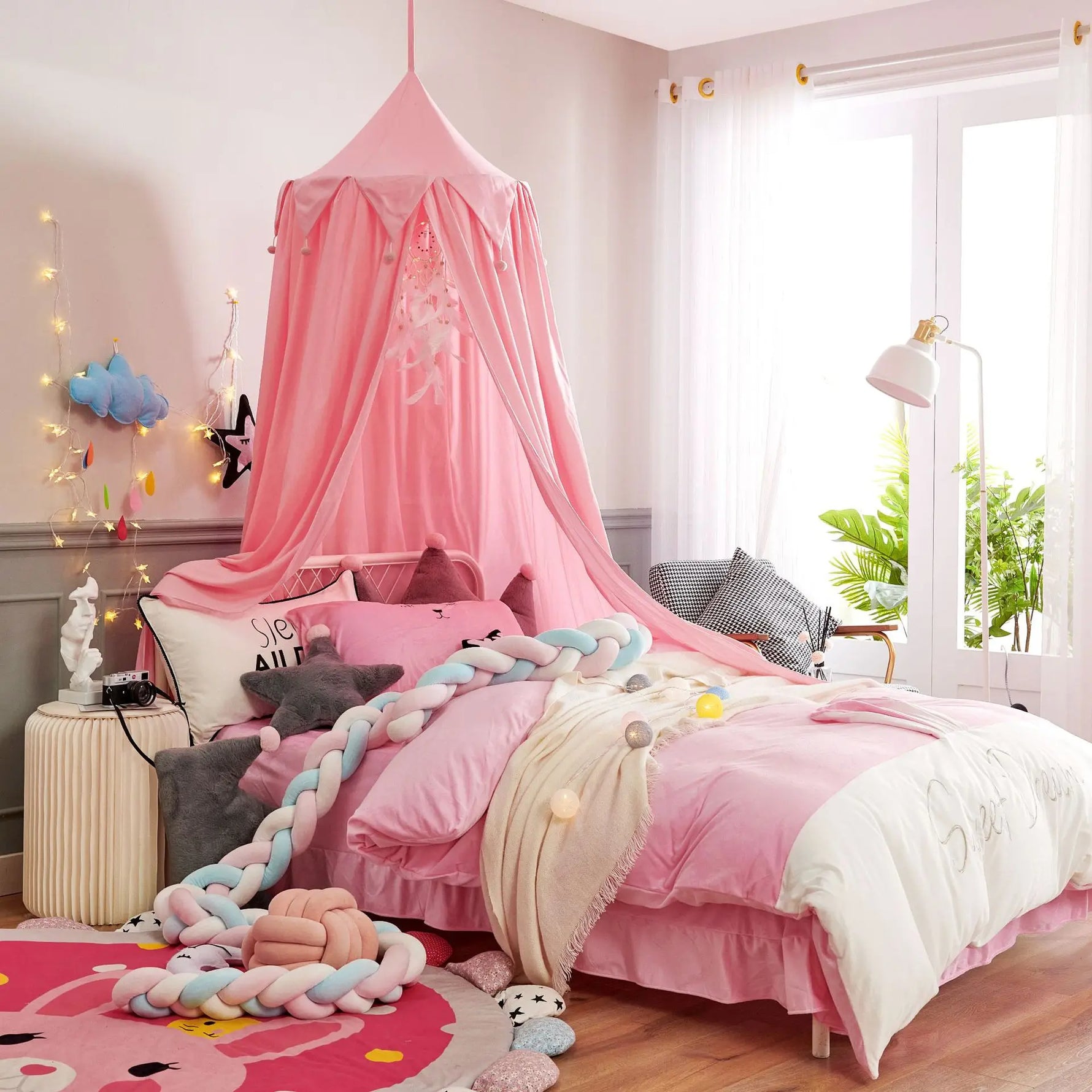 Une chambre de fille décorée avec des tons roses et pastel, avec un lit à baldaquin rose, des oreillers et couvertures moelleux, ainsi que des accessoires décoratifs.