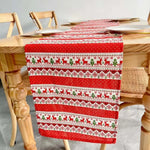 Un chemin de table de Noël rouge et blanc, orné de motifs de rennes et de flocons de neige, décorant une table en bois.