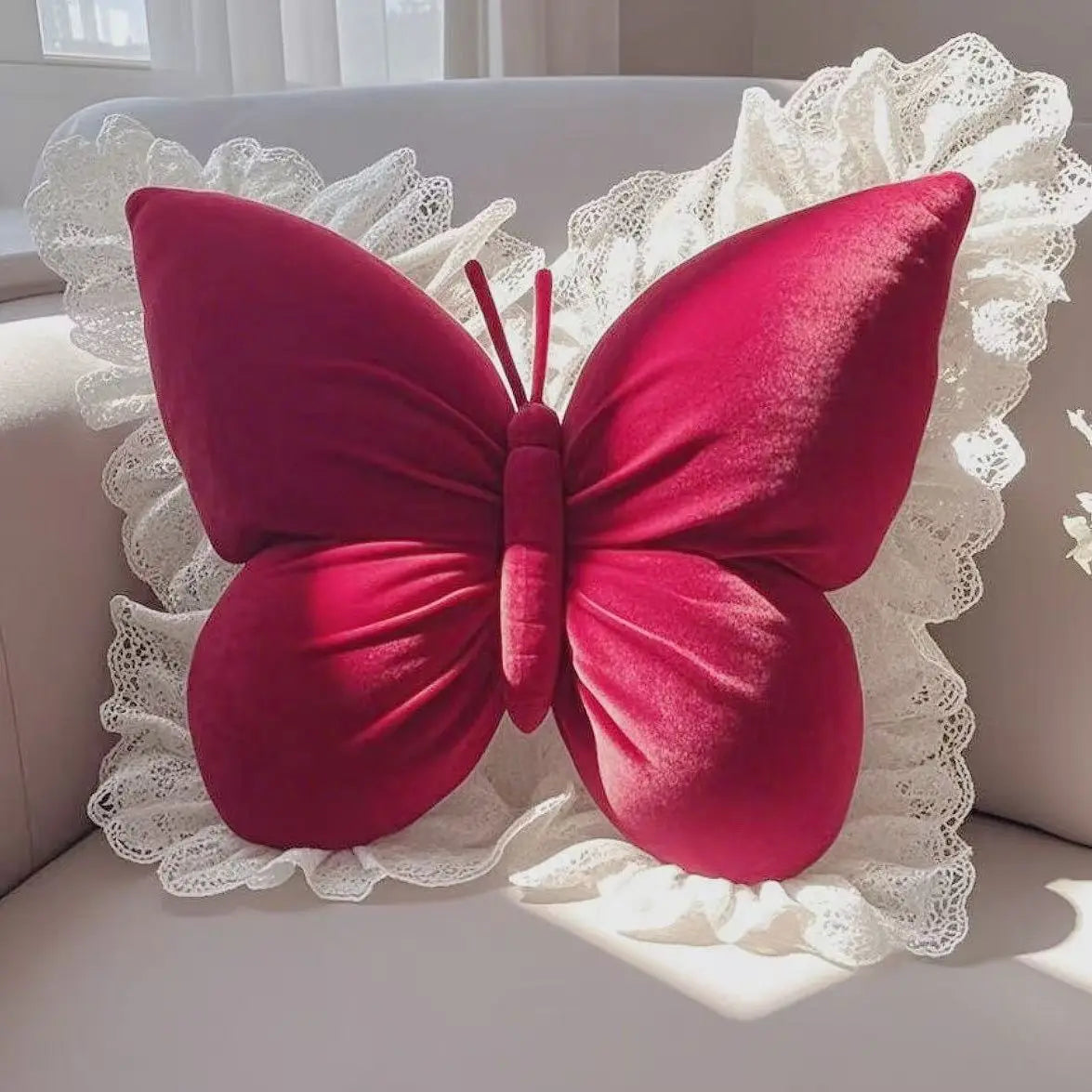 Un coussin décoratif en forme de papillon rouge vif, entouré de dentelle blanche, reposant sur une surface grise.