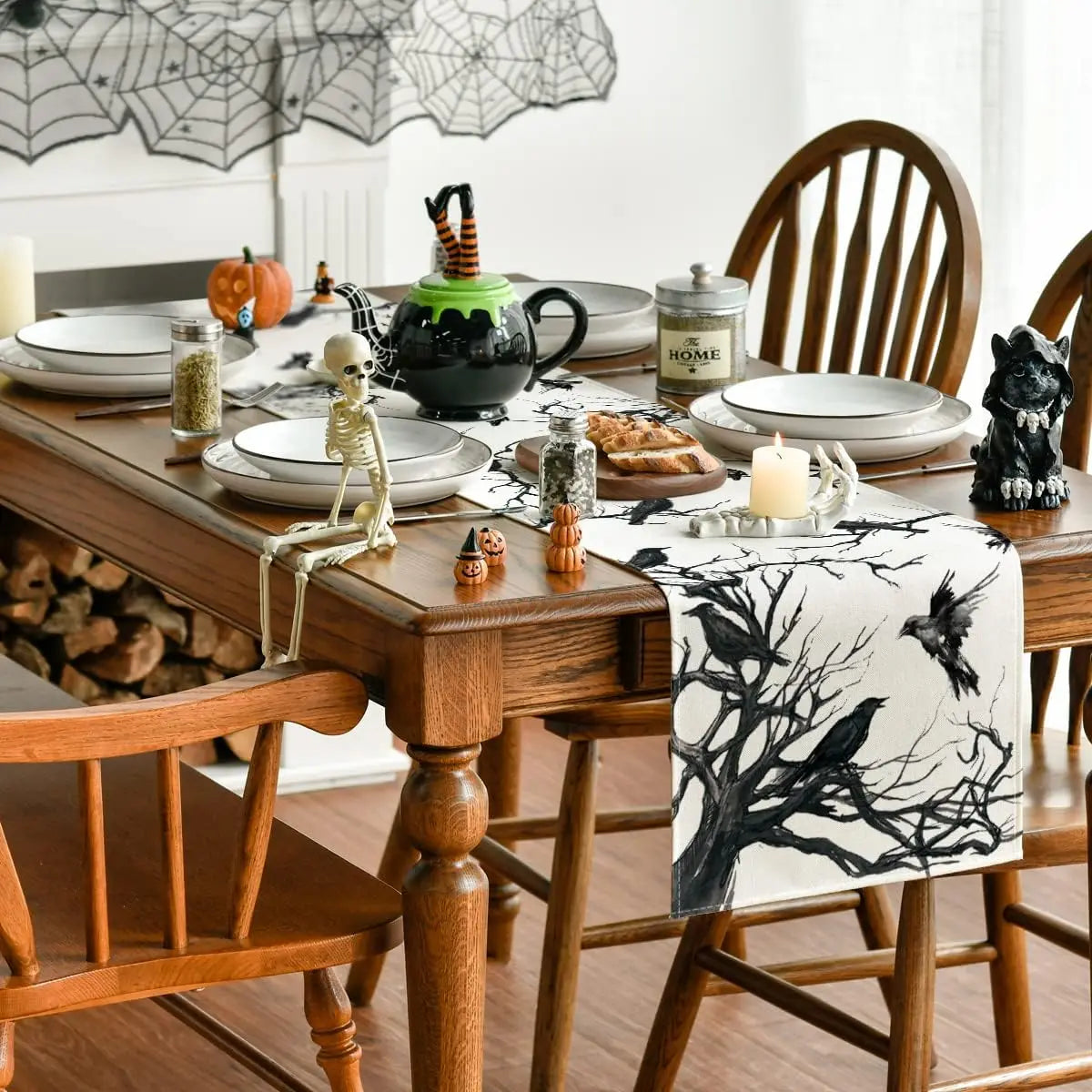Une table de salle à manger décorée pour l'Halloween, avec des assiettes blanches, une théière noire, des figurines de squelette et de chat, ainsi qu'un chemin de table orné de branches noires.