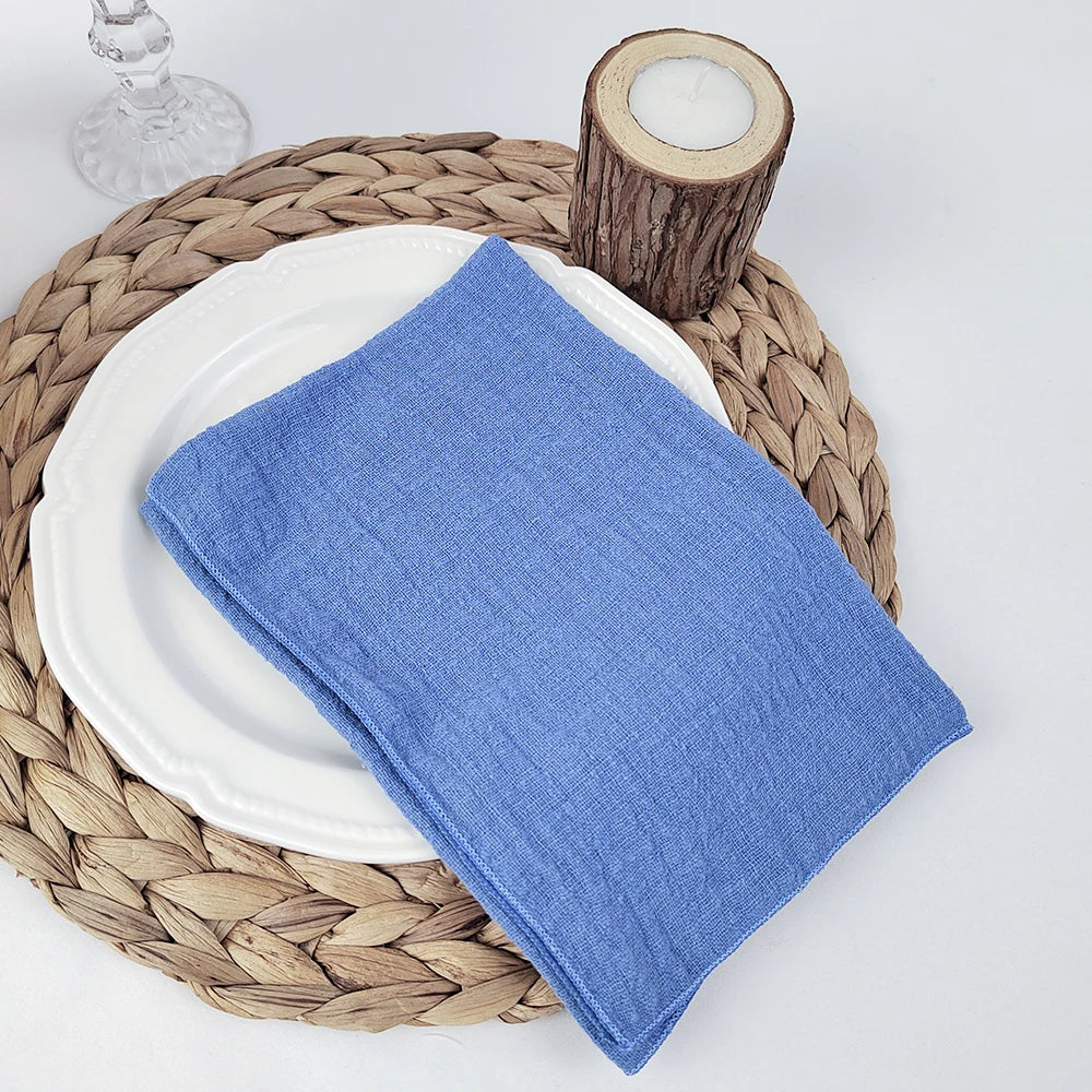 Un set de table en osier naturel, avec une assiette blanche et une serviette en tissu bleu, accompagné d'un photophore en bois.