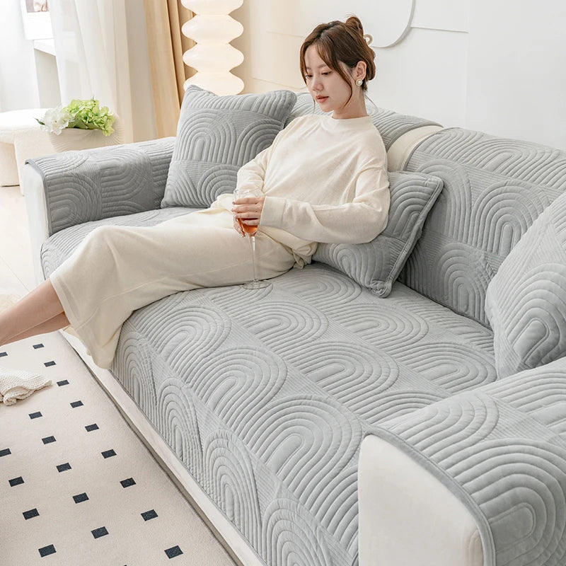 Une jeune femme vêtue de vêtements clairs se détend confortablement sur un canapé gris aux motifs ondulés, dans un intérieur lumineux.