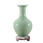 Vase en céramique vert de forme élégante reposant sur un socle en bois.