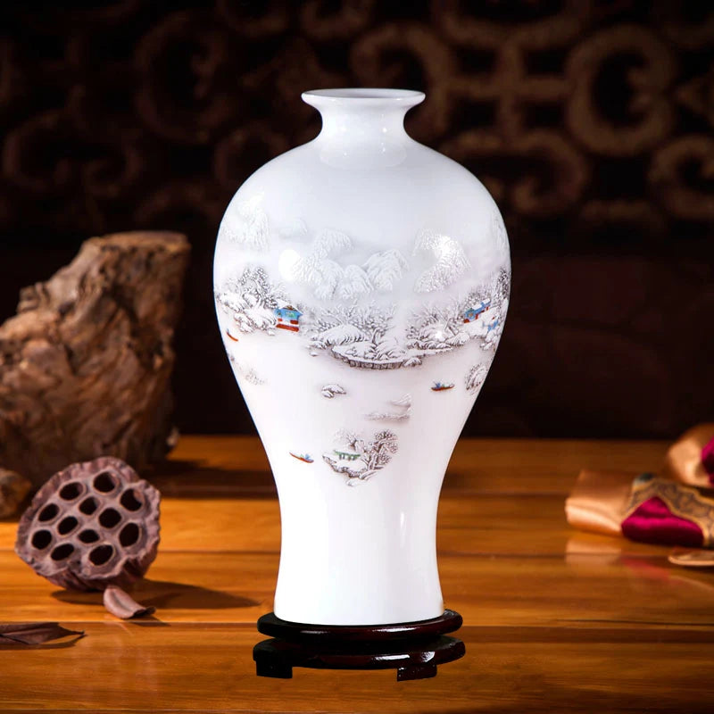 Ce vase en porcelaine blanche affiche une scène hivernale peinte avec finesse, représentant un paysage enneigé avec des maisons et des arbres dans une ambiance paisible et pittoresque.