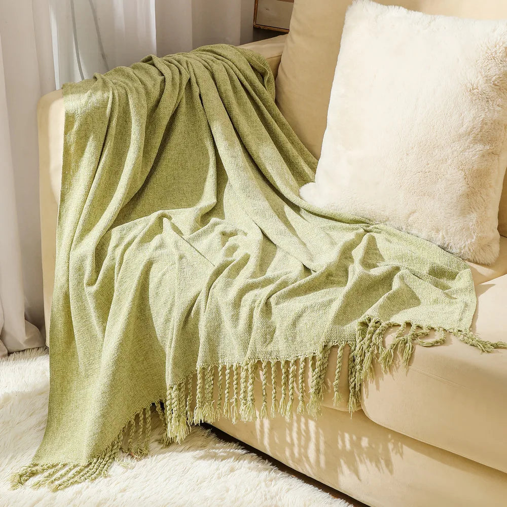 Une couverture en peluche verte décorative avec des franges élégantes, posée sur un canapé confortable.