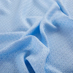 Texture en fil bleu pâle formant des motifs géométriques sur un tissu froissé.