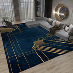 Ce salon moderne présente un tapis bleu foncé orné de motifs géométriques dorés, créant une ambiance élégante et sophistiquée. Le mobilier gris et les accents métalliques dorés complètent parfaitement la décoration.