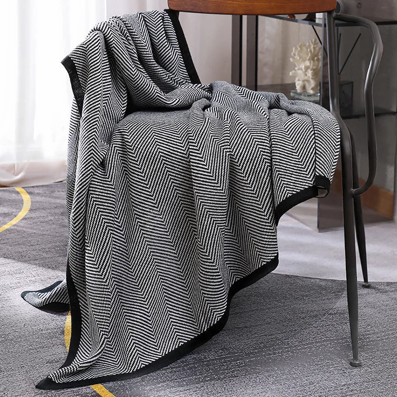 Une couverture rayée en noir et blanc, élégamment posée sur un fauteuil en bois, crée une ambiance chaleureuse et sophistiquée dans cette pièce moderne.
