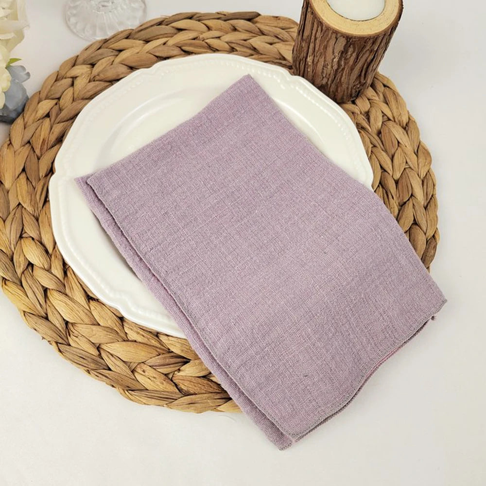 Serviette en lin lavande posée sur un plateau tressé, accompagnée d'un vase de bois.