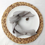 Un châle gris doux et confortable posé sur une assiette blanche, entouré d'un dessous de plat tressé en fibres naturelles.