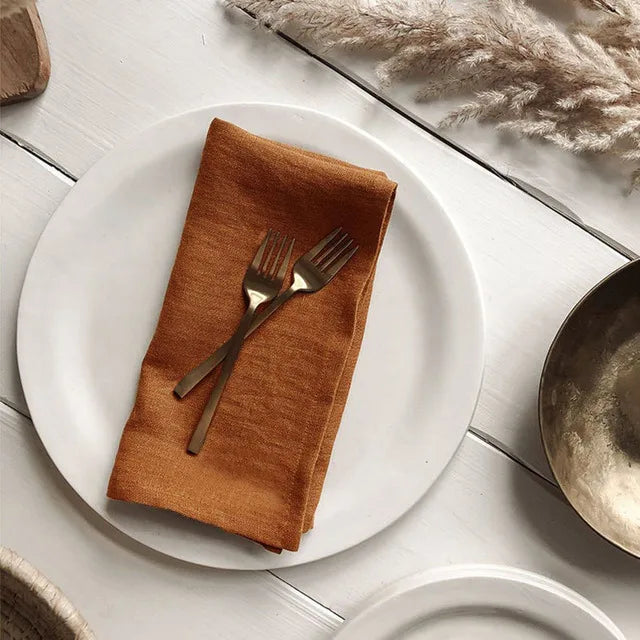 Un arrangement élégant de fourchette et couteau sur une serviette marron, posé sur une assiette blanche, avec des décorations végétales autour.