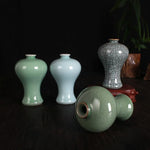 Assortiment de vases en céramique dans des teintes vertes et craquelées, avec un élément de décor en rouge-brun, sur un fond sombre.