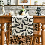 Cette image représente un cadre décoratif en noir et blanc avec des motifs de chauves-souris, placé sur une étagère en bois avec différents objets d'Halloween comme des squelettes, des citrouilles et une peluche de chat noir.