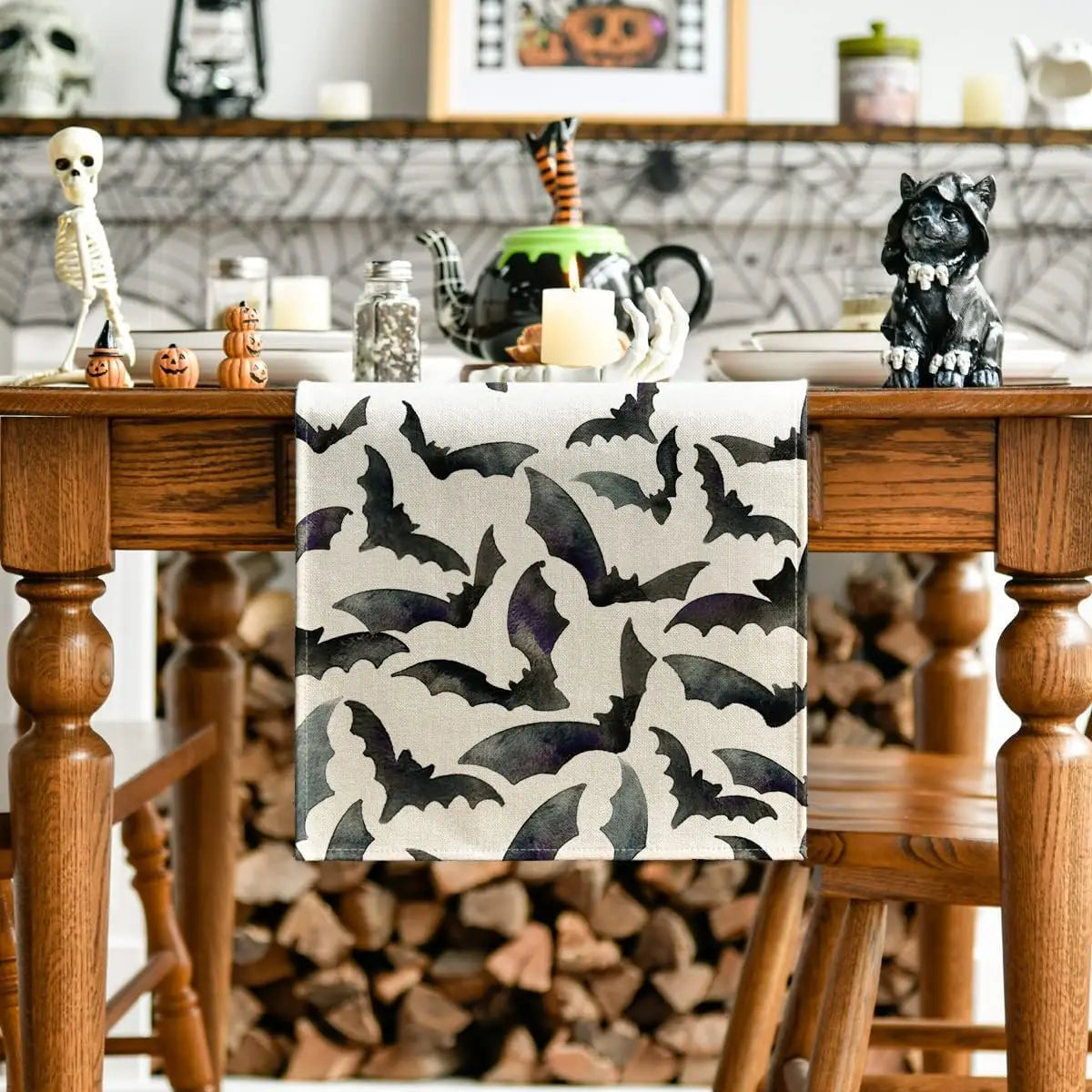 Cette image représente un cadre décoratif en noir et blanc avec des motifs de chauves-souris, placé sur une étagère en bois avec différents objets d'Halloween comme des squelettes, des citrouilles et une peluche de chat noir.
