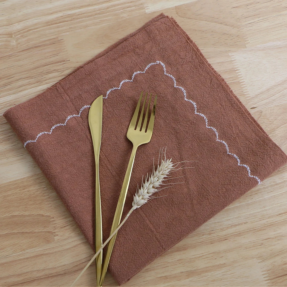 Une serviette en tissu brun et des couverts en métal doré sont disposés sur une surface en bois.