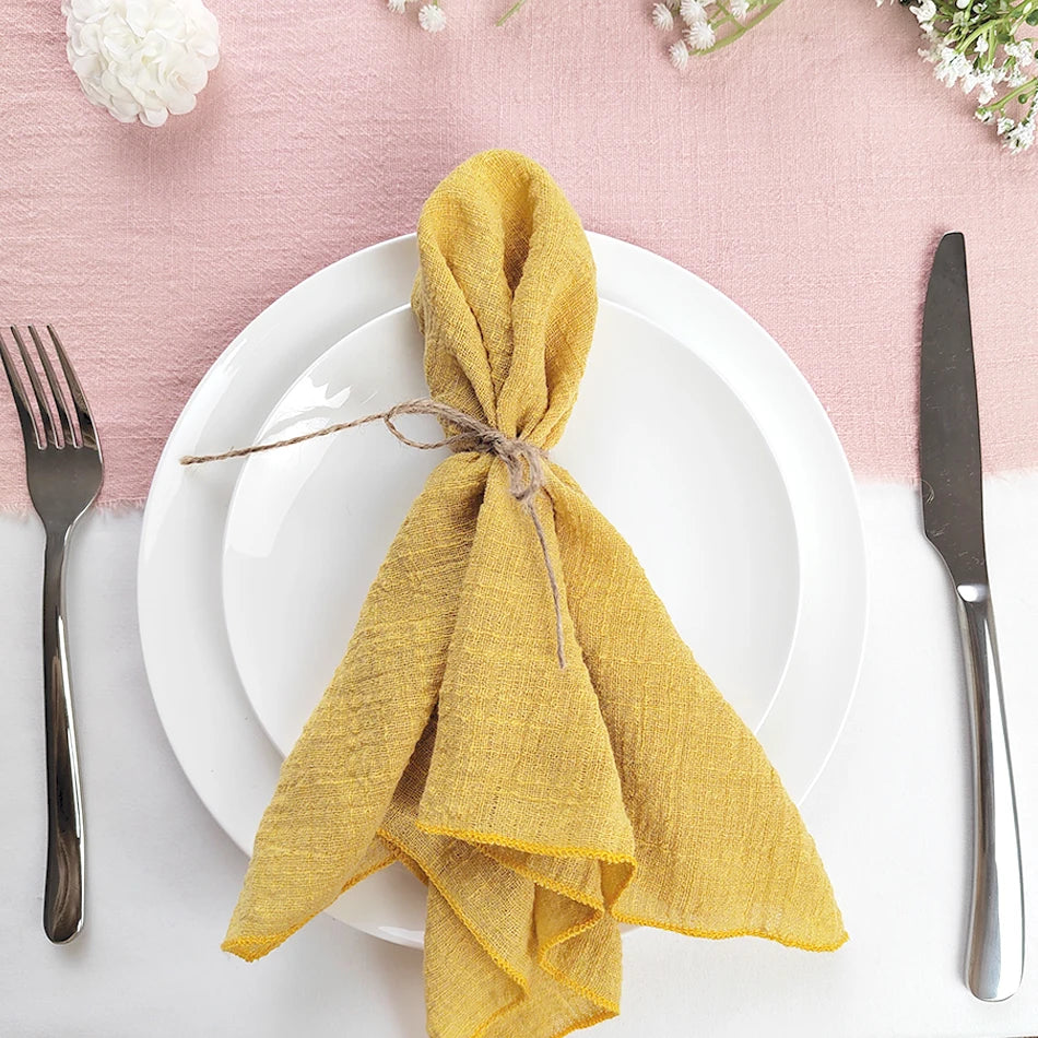 Une élégante serviette jaune nouée sur une assiette blanche, avec des couverts argentés, sur un fond rose doux.