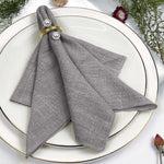 Serviette grise avec anneaux dorés, posée sur une assiette blanche, entourée de fleurs et de feuillage décoratifs.