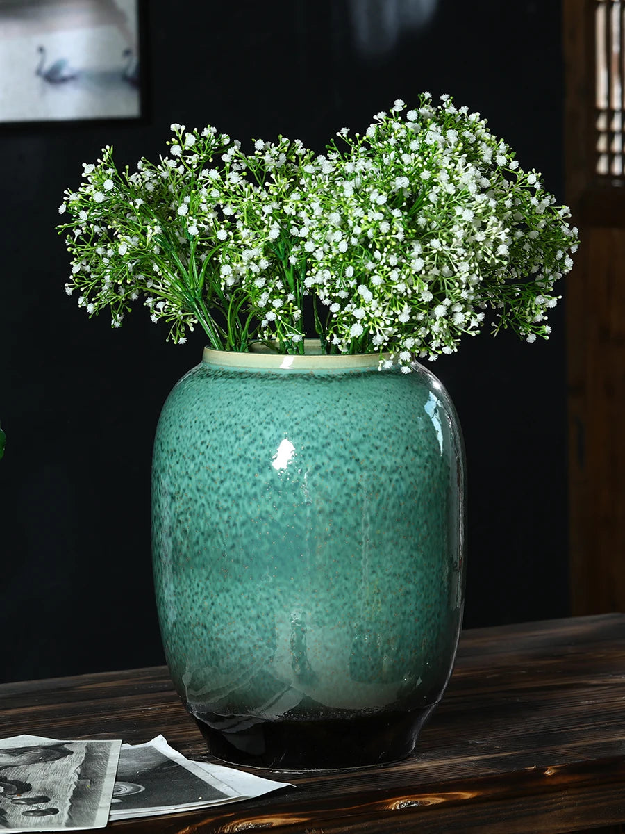 Un bouquet de fleurs blanches repose dans un vase en céramique vert, créant une scène élégante et naturelle sur un fond sombre.