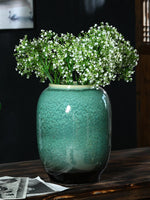 Un bouquet de fleurs blanches repose dans un vase en céramique vert, créant une scène élégante et naturelle sur un fond sombre.