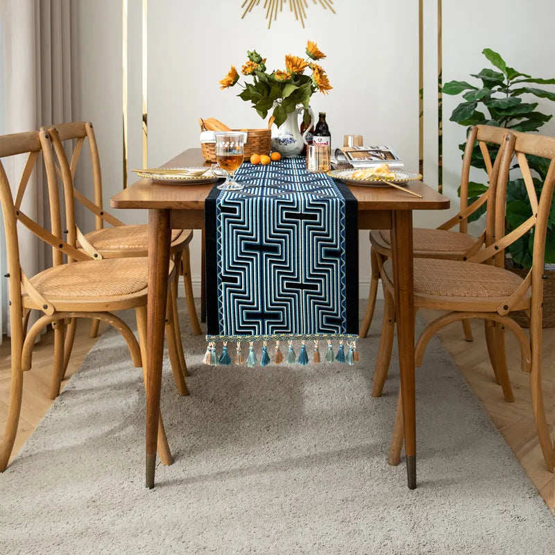 Une élégante table à manger avec des fleurs de tournesol dans un vase, des articles de décoration et un chemin de table à motifs géométriques bleus et blancs.