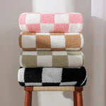 Des serviettes de bain aux motifs géométriques colorés empilées sur un tabouret en bois.